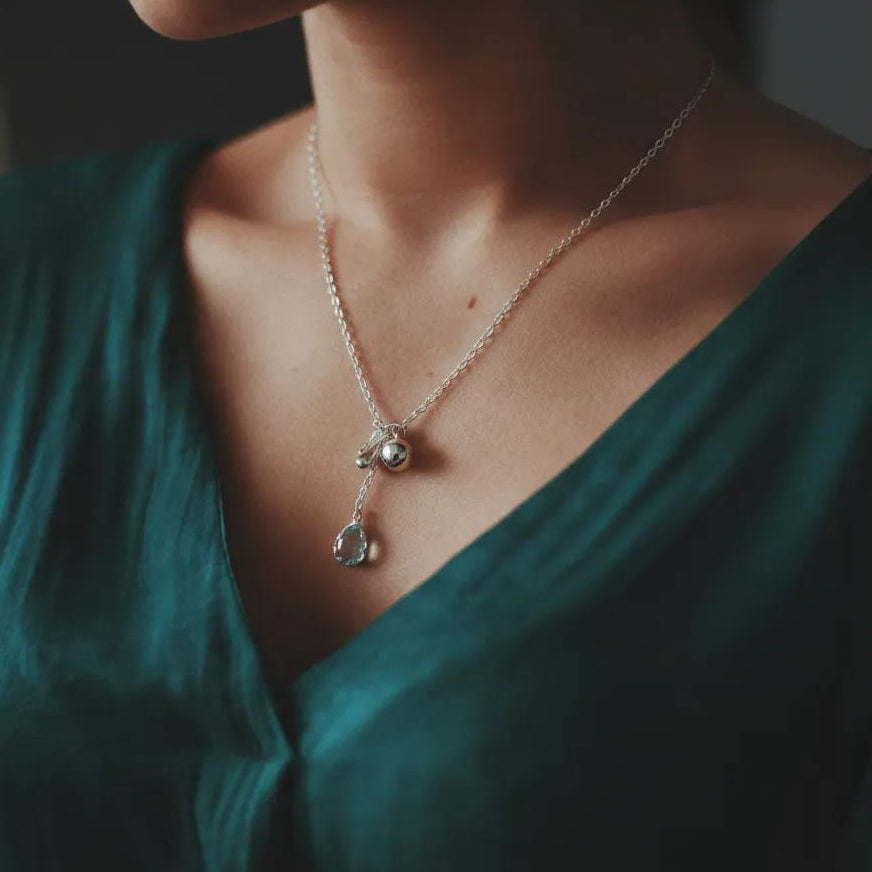 Amara Jewels sterling silver necklace with a blue teardrop gemstone pendant and silver charms.