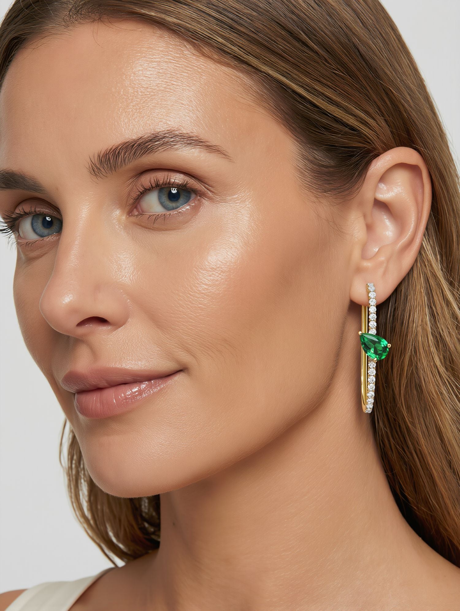 Close-up of a woman wearing emerald green earrings with a white background