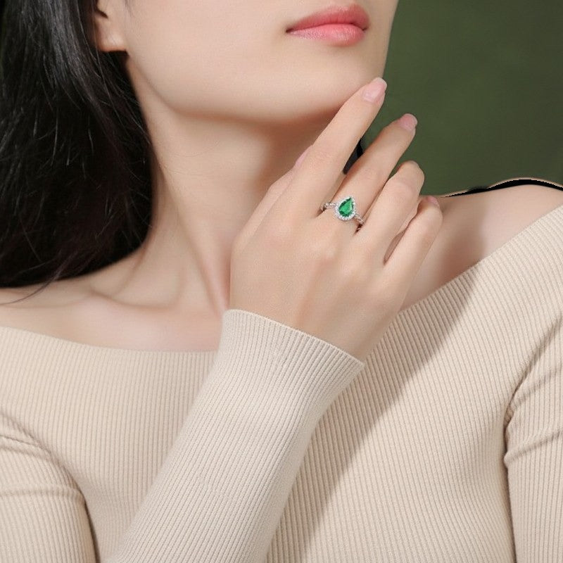 Amara Jewels sterling silver ring with a green teardrop gemstone surrounded by small clear stones. Intricate detailing on band.