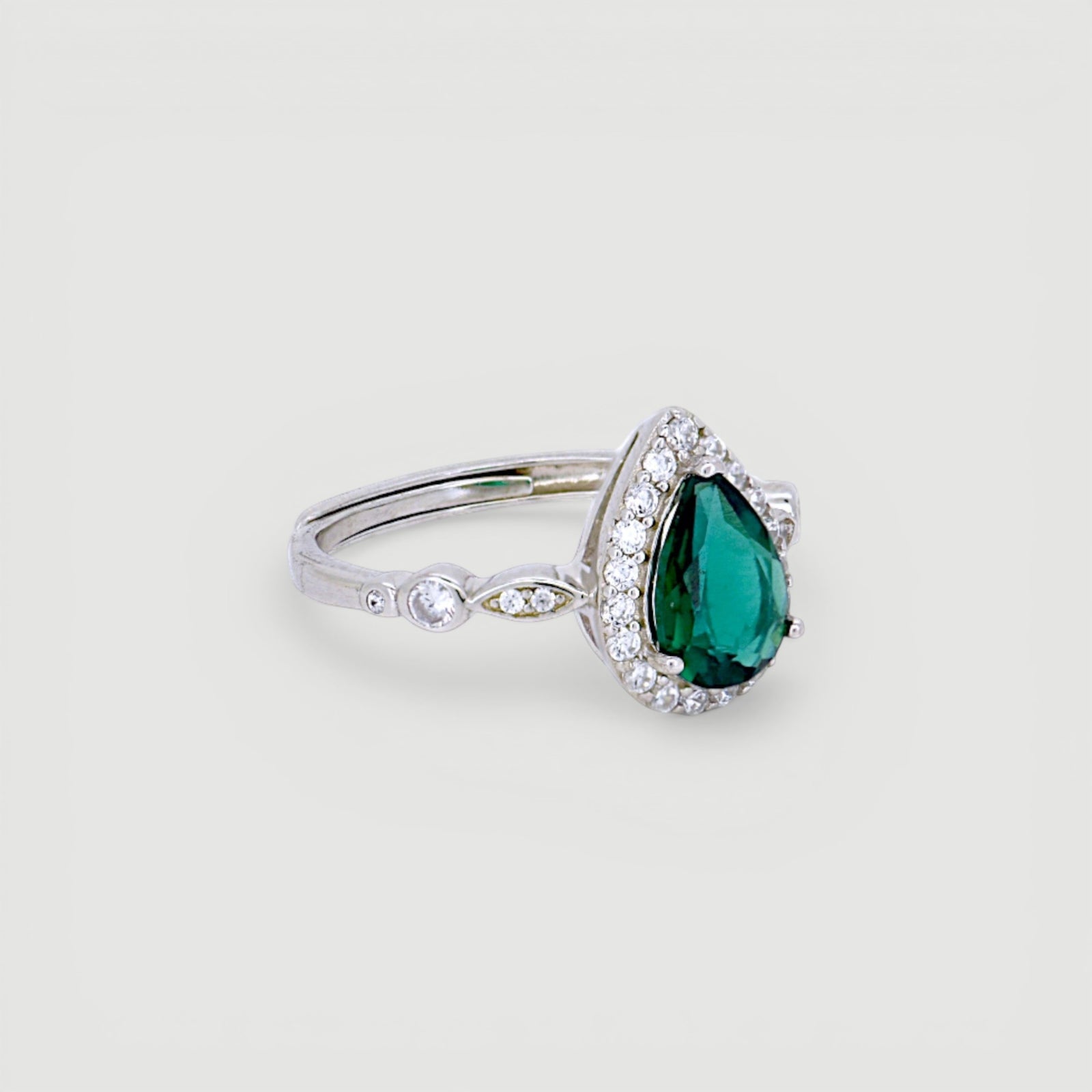 Amara Jewels sterling silver ring with a green teardrop gemstone surrounded by small clear stones. Intricate detailing on band.