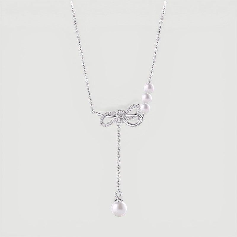 Amara Jewels sterling silver necklace with cubic zirconia bow and trio of white pearls and dangling single pearl drop.