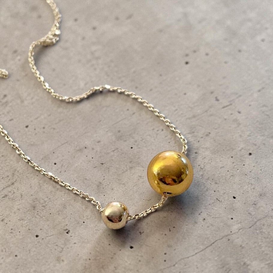Amara Jewels two-tone sphere pendant necklace with polished silver chain, featuring a large gold sphere and a smaller silver sphere.