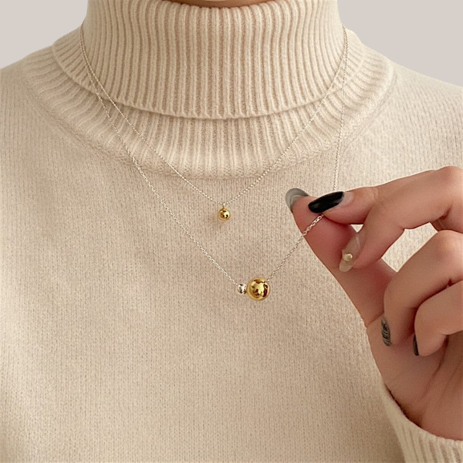 Amara Jewels two-tone sphere pendant necklace with polished silver chain, featuring a large gold sphere and a smaller silver sphere.